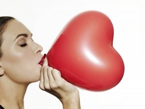 Girl blowing up a red heart shaped balloon