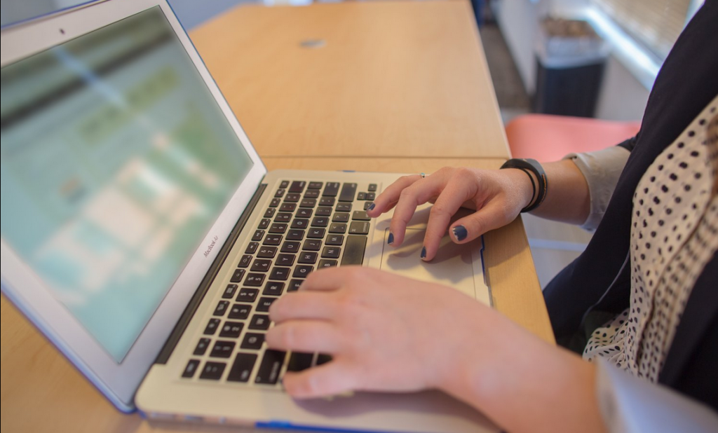 person with nail polish, polka dot shirt, and blazer working and typing on laptop for miss millennia internship and full-time job