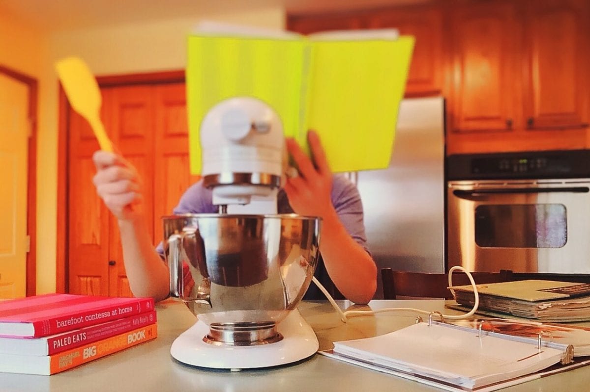person holding cookbook and spatula with mixer