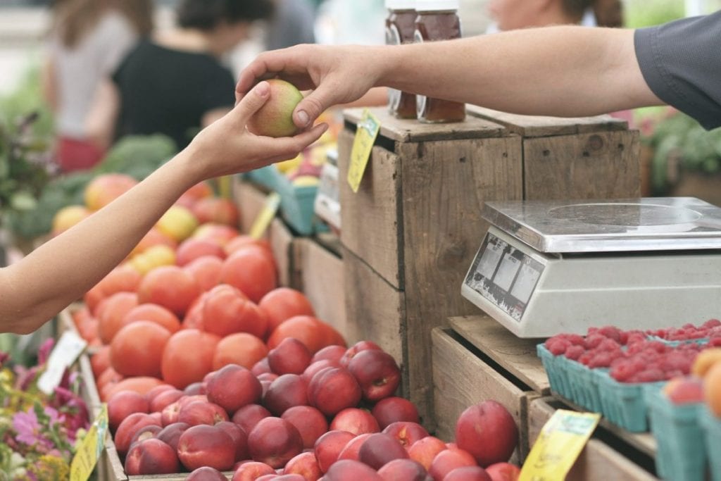 man handing woman an apple at a fruit stand