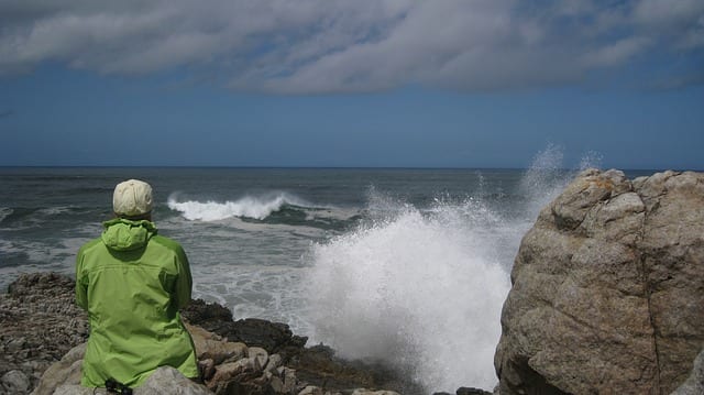 person sitting on rock looking at ocean