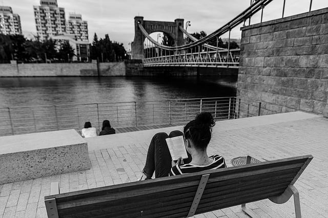 woman reading by river and bridge