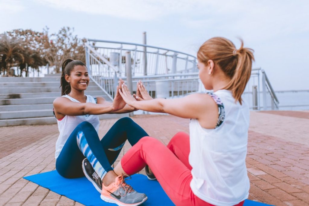two women on ground working out together outside