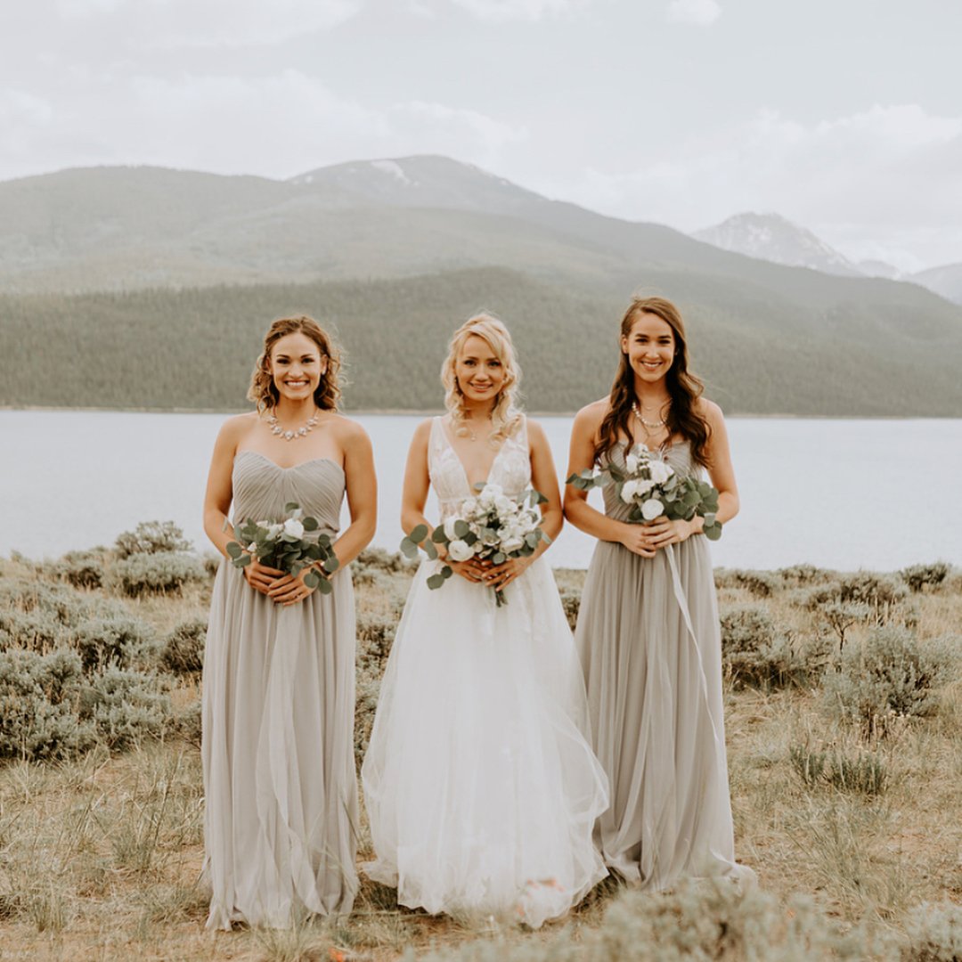 bride standing between two bridesmaids near lake