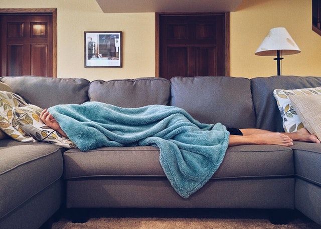 person lying on couch under blanket