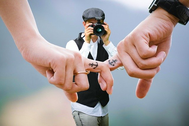 photographer taking a picture of two people linking fingers with anchor tattoos