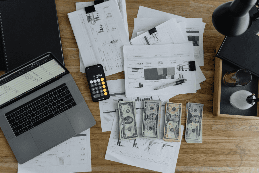 A desk with papers, cash, and a laptop on top