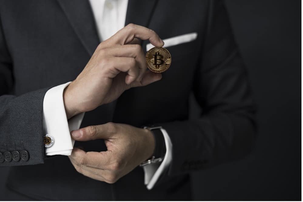 A person in a suit holding a Bitcoin