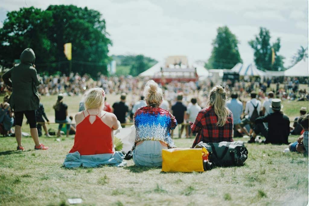 Three women sitting on a lawn during a music festival