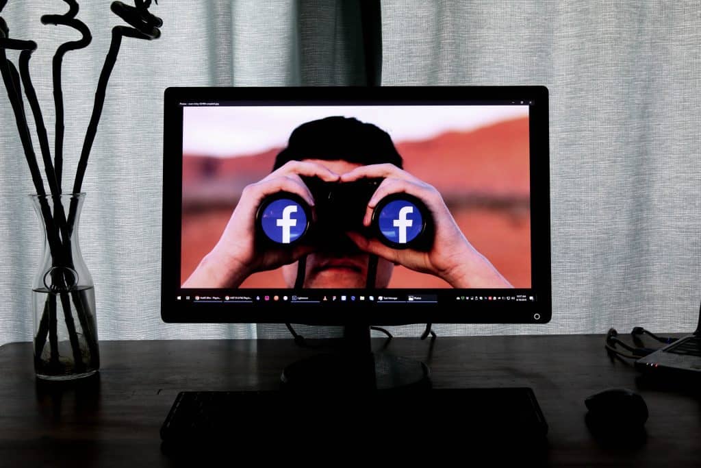 A person on a computer screen looking through binoculars with the facebook logo