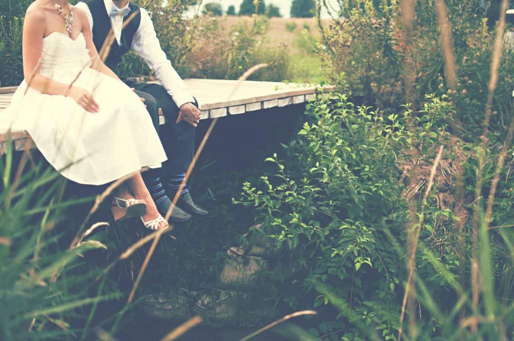 A newly wedded couple sitting on the edge of a bridge 