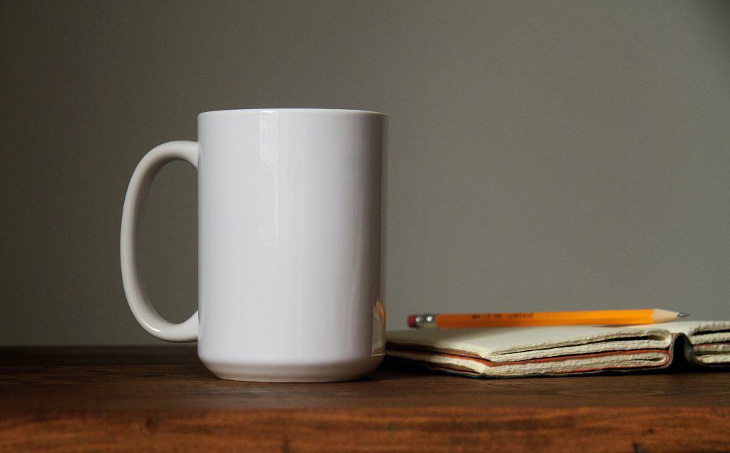 A coffee cup next to a journal and pencil