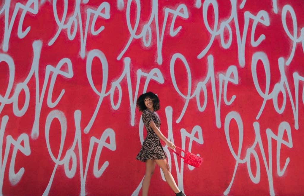 A woman walking in front of a wall with love written over and over again on the wall behind her.
