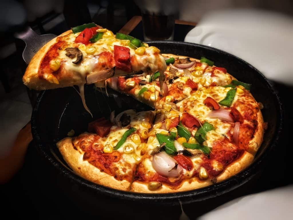 A slice of pizza being lifted with veggies on top