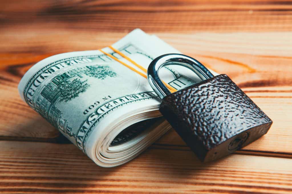 A wad of cash sitting on a wooden table with a lock on top