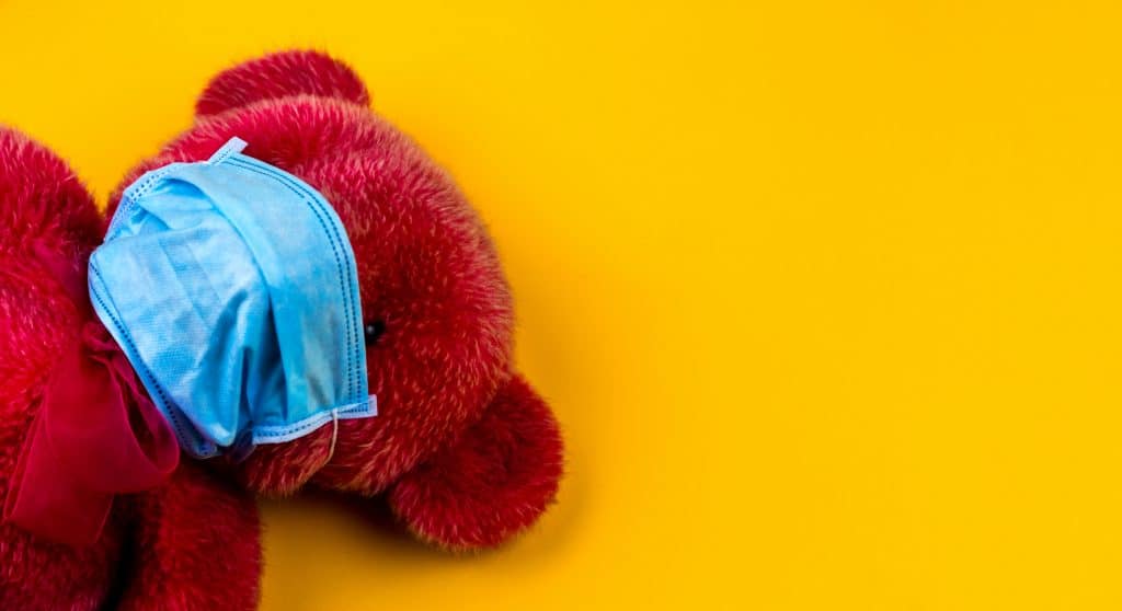 A red teddy wearing a face mask in front of a yellow background