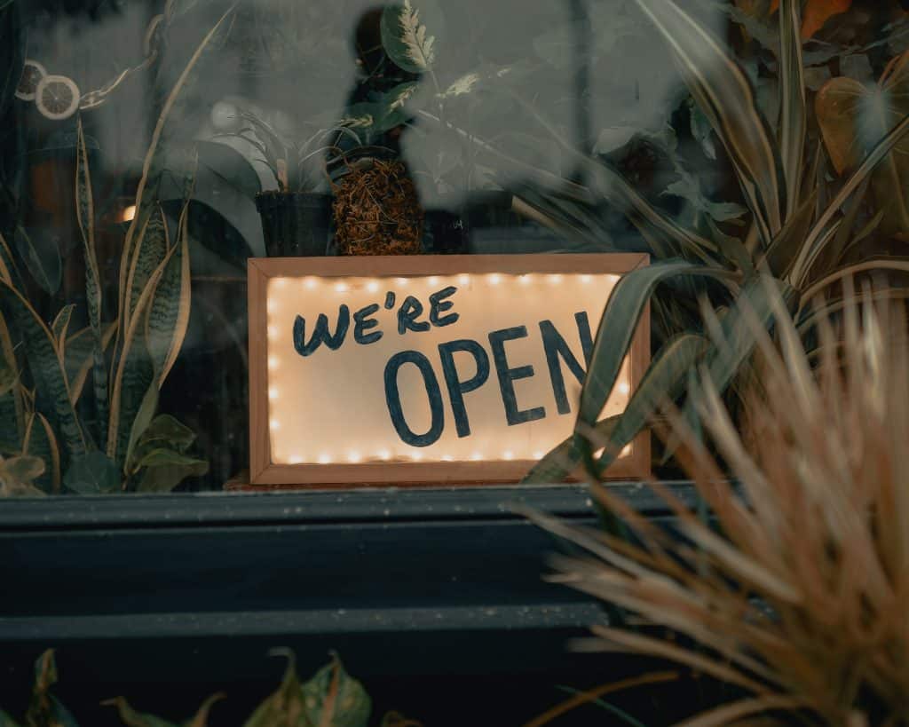 A "we're open" sign in a business' window surrounded by plants 
