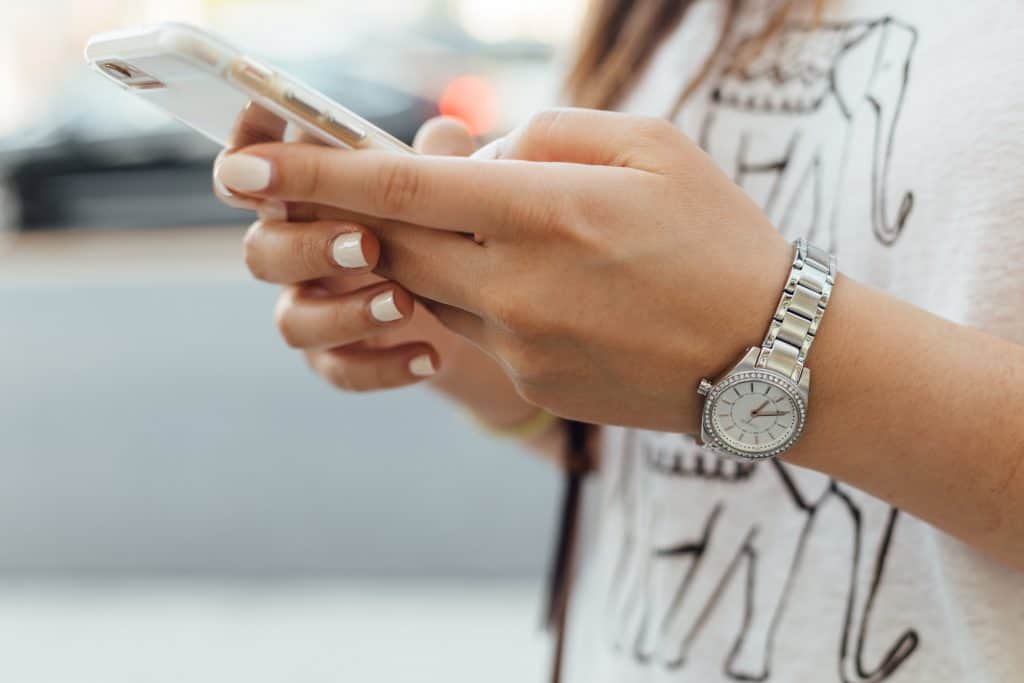 A person, wearing a watch and have painted nails, on their phone. 