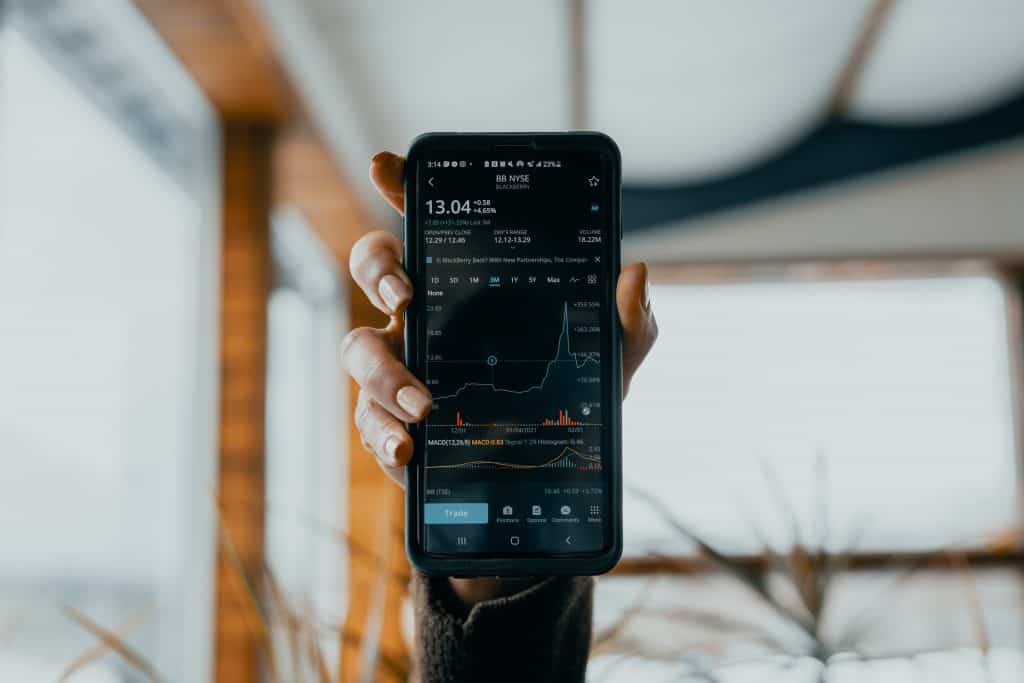 A manicured hand holding a phone showing stocks